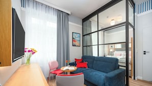 Una sala de estar moderna con un sofá azul, una mesa de comedor de madera y una pequeña mesa redonda con un libro y flores.