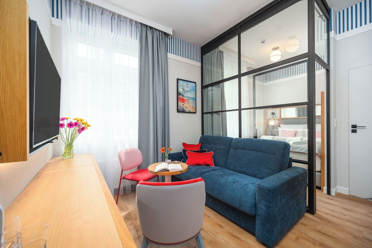 Ein modernes Wohnzimmer mit einem blauen Sofa, einem Holzesstisch und einem kleinen runden Tisch mit Buch und Blumen.