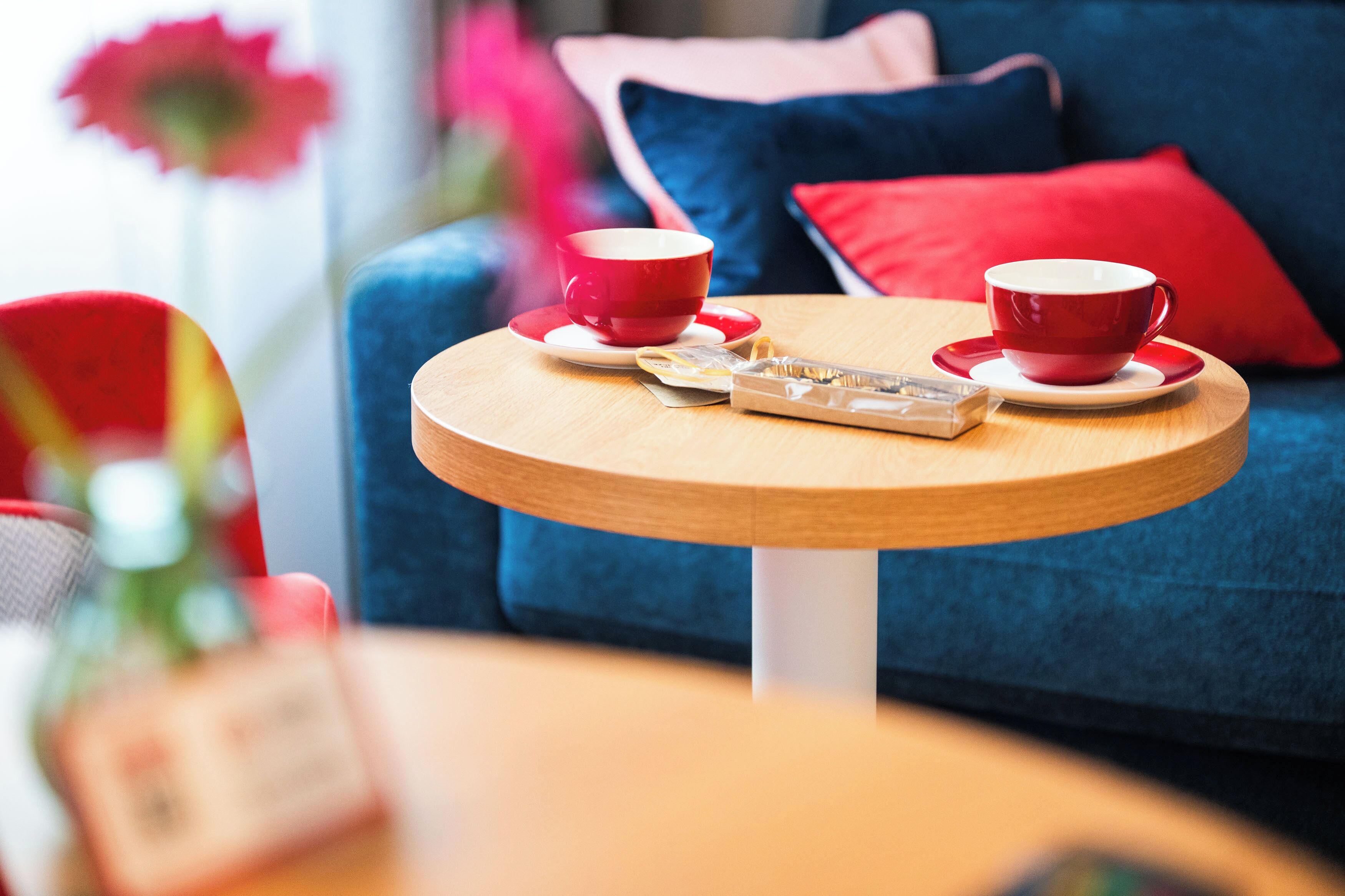 Een ronde houten tafel met twee rode kopjes en schotels, zakdoekjes en een klein dienblad.