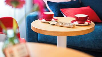 Een ronde houten tafel met twee rode kopjes en schotels, zakdoekjes en een klein dienblad.