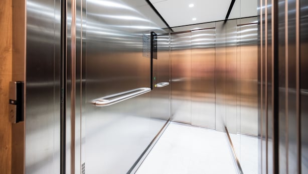 Ascensor vacío con paredes metálicas y una puerta de madera.