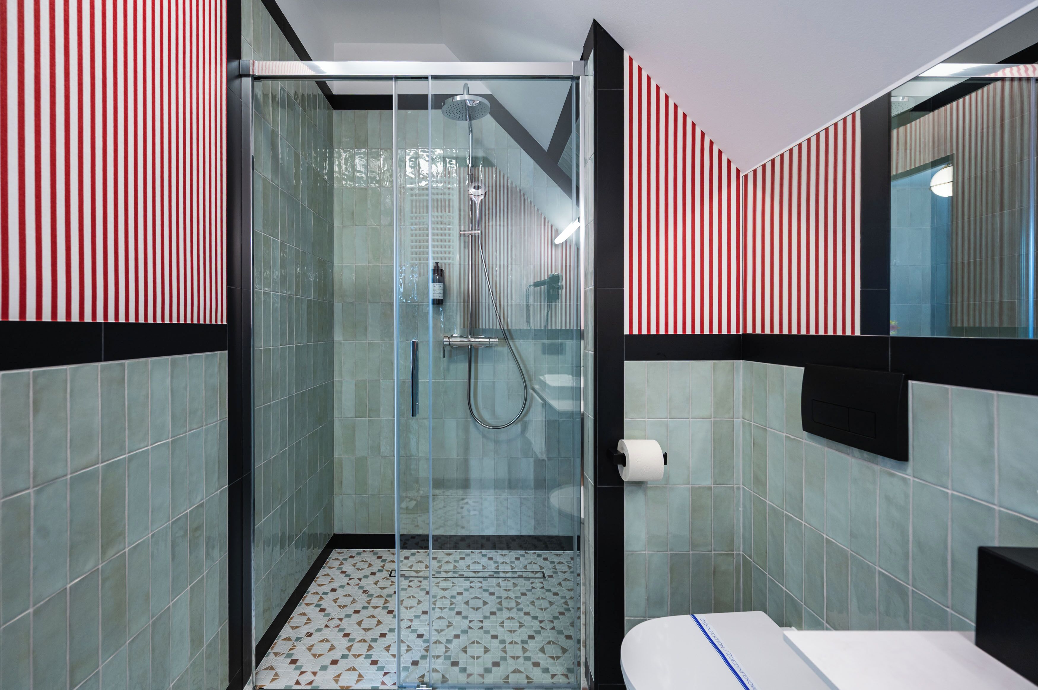 A modern bathroom with a glass-enclosed shower, tiled walls, and a toilet with a paper towel dispenser.