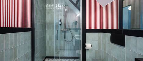 A modern bathroom with a glass-enclosed shower, tiled walls, and a toilet with a paper towel dispenser.