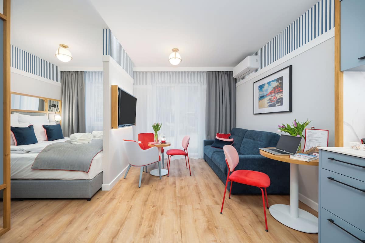 Ein modernes Hotelzimmer mit Bett, Schreibtisch mit Laptop, Sofa und Essecke mit Stühlen.