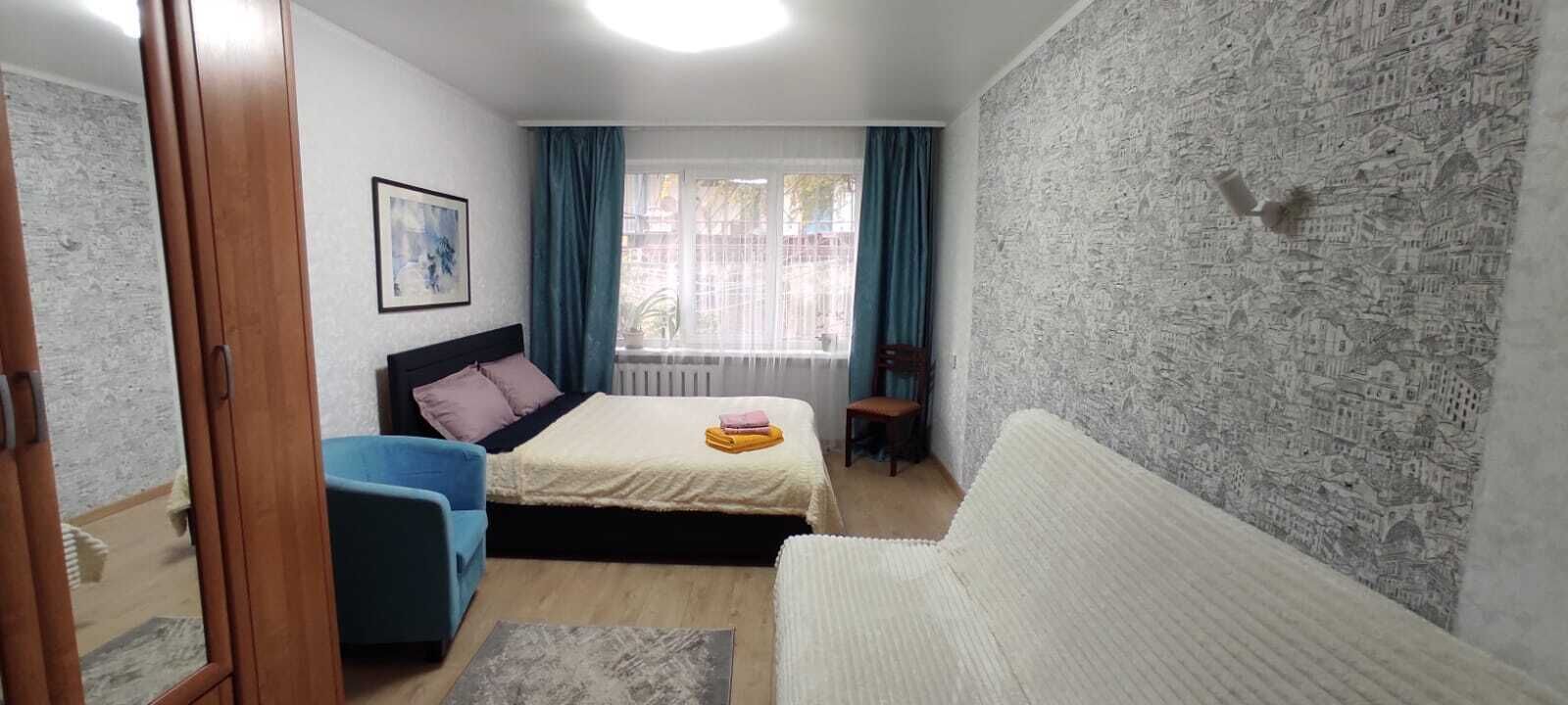 Un dormitorio con cama, una silla azul, un sofá blanco, una ventana con cortinas y una pared con textura.
