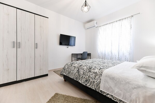 Une chambre à coucher avec un lit, une télévision, une armoire et une fenêtre avec des rideaux.