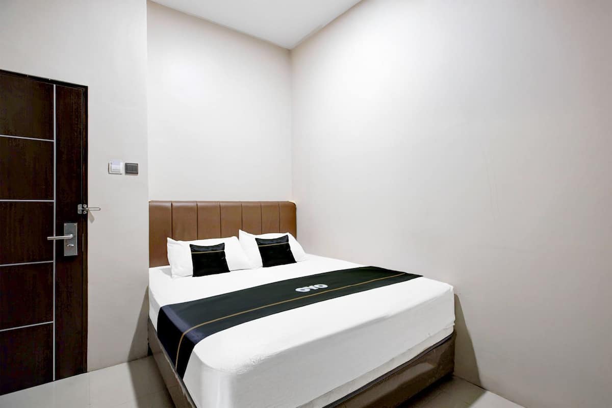 A hotel room with a bed, a wooden door, and a white wall.