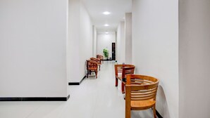 A hallway with wooden chairs and tables, white walls, and a ceiling with recessed lighting. - Hotel O Balikpapan near Siloam Hospital formerly Syafla Guest House (Balikpapan)