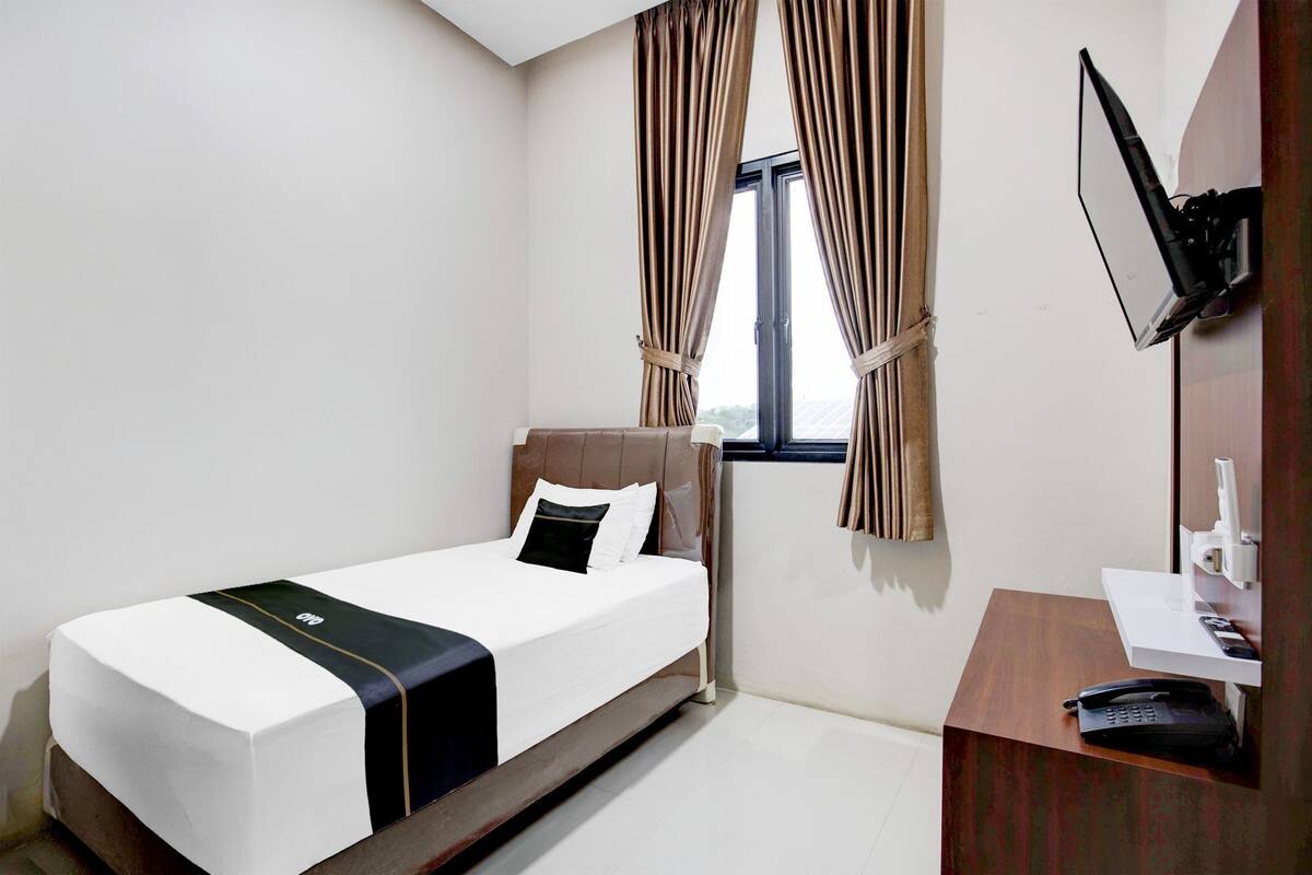 A hotel room with a bed, a desk, a television, and curtains.