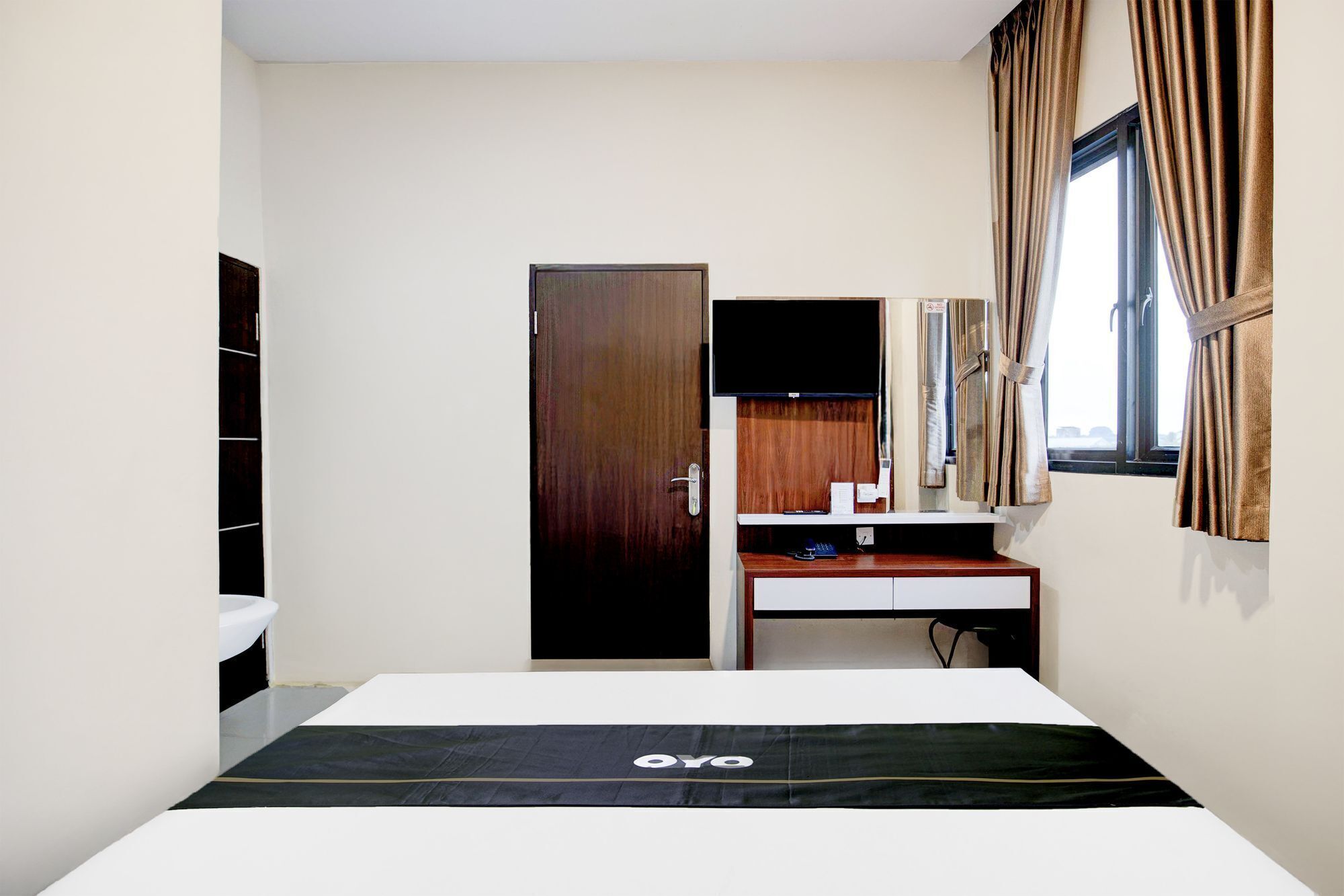 Una habitación de hotel con cama, escritorio, espejo, televisor y ventana con cortinas.
