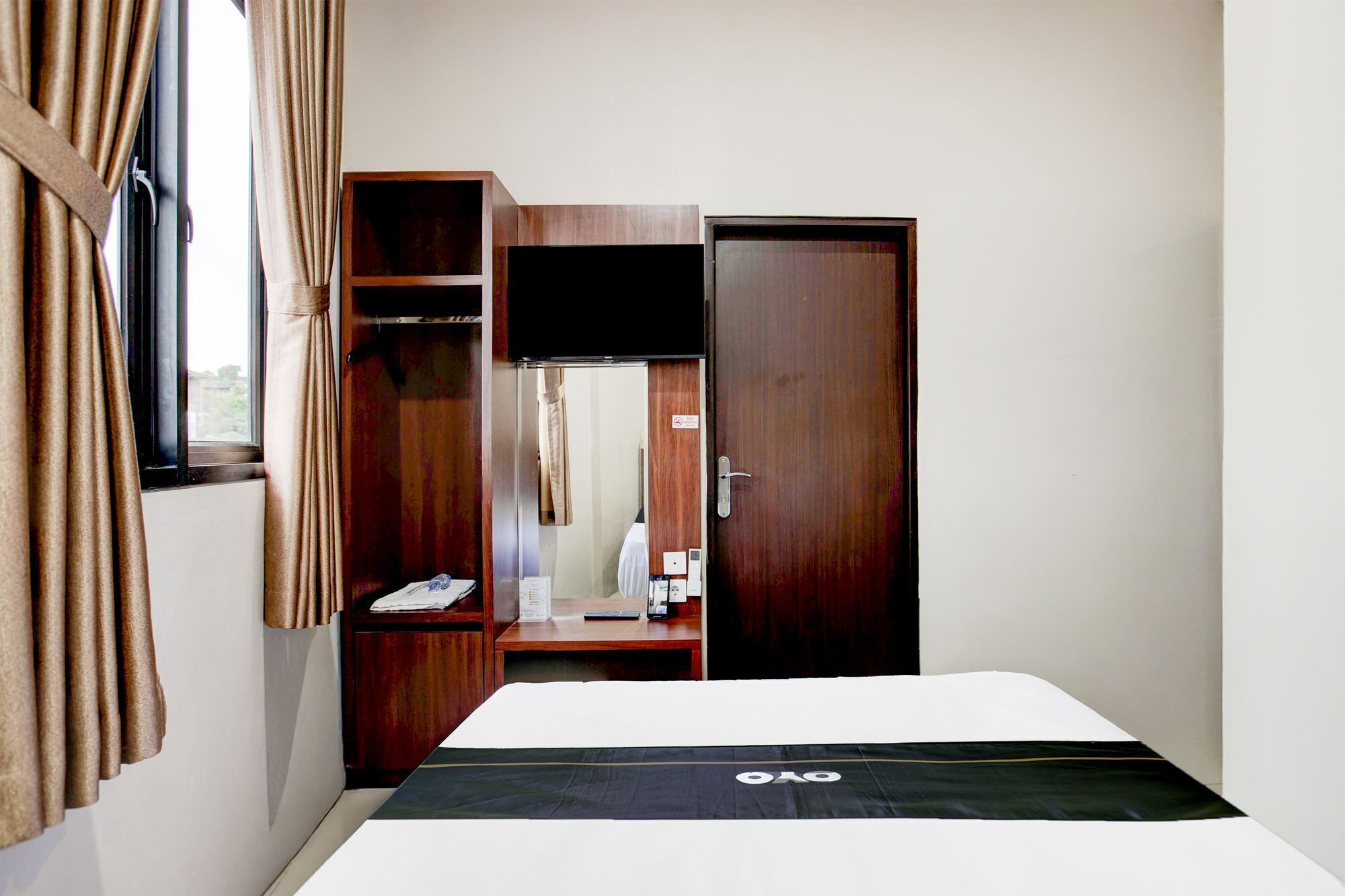 A hotel room with a bed, a wardrobe, a desk with a mirror, and a window with curtains.
