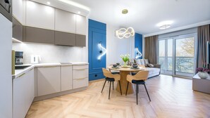 Una cucina moderna con mobili bianchi, una parete decorata in blu e un'area pranzo con tavolo e sedie in legno.