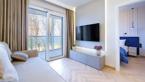 Una moderna camera d'hotel con un letto grande, una TV fissata al muro, una porta scorrevole in vetro verso l'esterno e un comodino con un vaso di fiori.