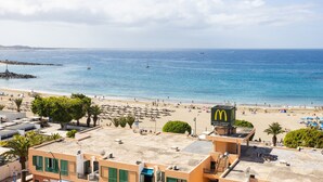 A beach with a McDonald's restaurant, a rocky breakwater, and a clear blue sea. - Stunning sea view apt in Los Cristianos (Los Cristianos)