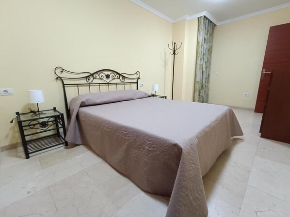 Un dormitorio con una cama, una mesita de noche, una lámpara y un perchero.