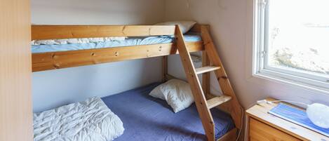 A bunk bed with a ladder, a desk with a chair, and a window with a view.