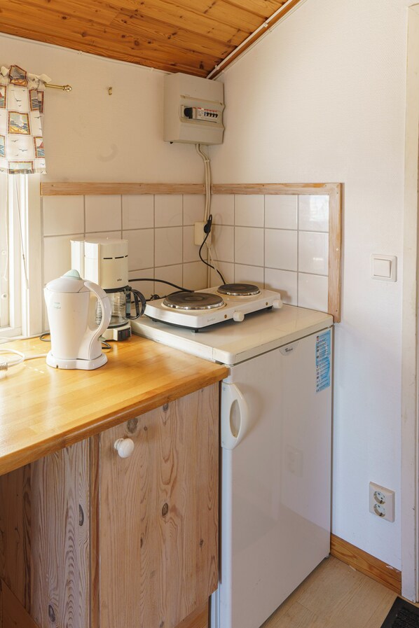 A compact kitchen with a wooden countertop, a white refrigerator, a coffee maker, and a small electric stove. - Femöre Marina (Oxelosund)