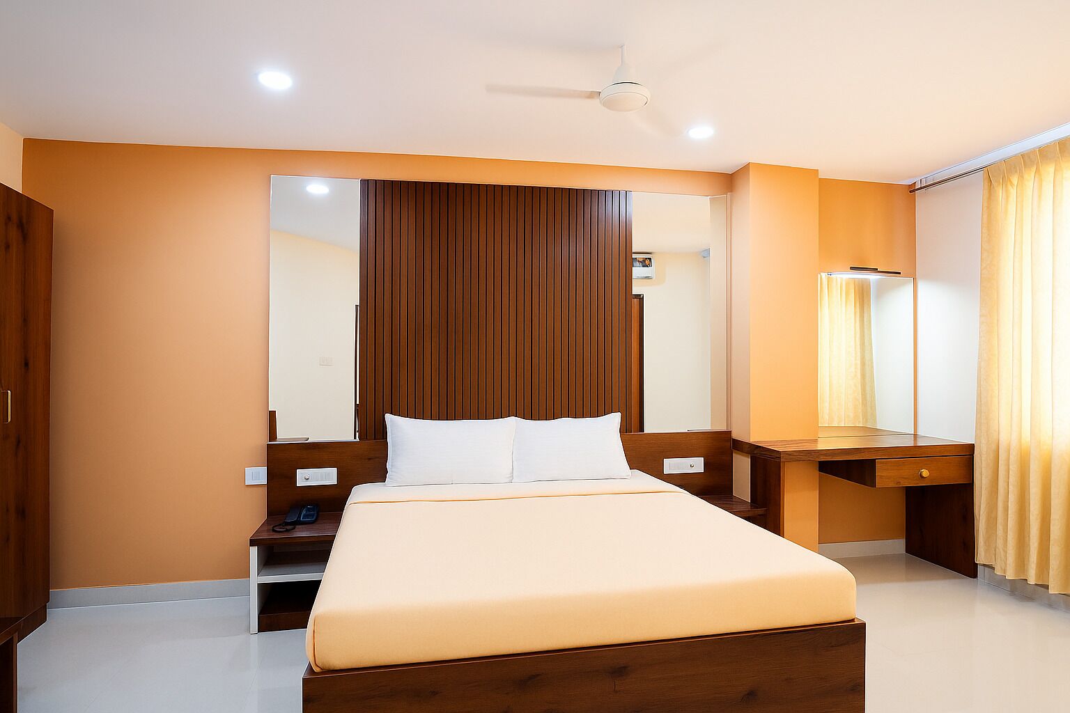 A modern hotel room with a large bed, wooden headboard, a bedside table with a lamp, and a mirror.