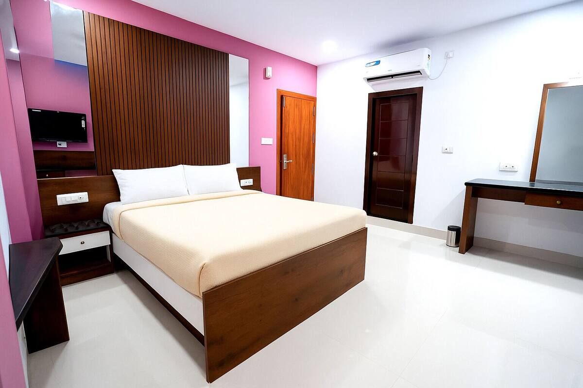 Un dormitorio moderno con una cama de madera, un televisor, un escritorio y un equipo de aire acondicionado.