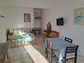 A bedroom with a bed, a desk, a chair, a TV, and a painting on the wall.