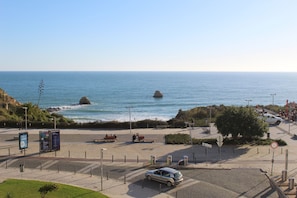 A coastal road with a car parked on the side, a pedestrian walkway, and a view of the sea with rocks. - Praia Rocha Balcony First Line Beach View Studio (Portimão)
