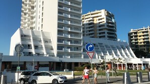 A modern high-rise hotel with multiple balconies, a pedestrian area with a directional sign, and a parking lot with cars. - Praia Rocha Balcony First Line Beach View Studio (Portimão)