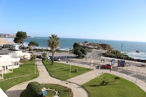 A coastal promenade with a clear view of the sea, a paved walkway, and a small landscaped area with a fountain. - Praia Rocha Balcony First Line Beach View Studio (Portimão)