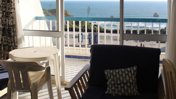 A balcony with a view of the ocean, a white table, and a dark-colored sofa with a patterned pillow. - Praia Rocha Balcony First Line Beach View Studio (Portimão)