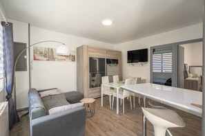 Et moderne opholdsrum med sofa, spisebord og tv på væggen.