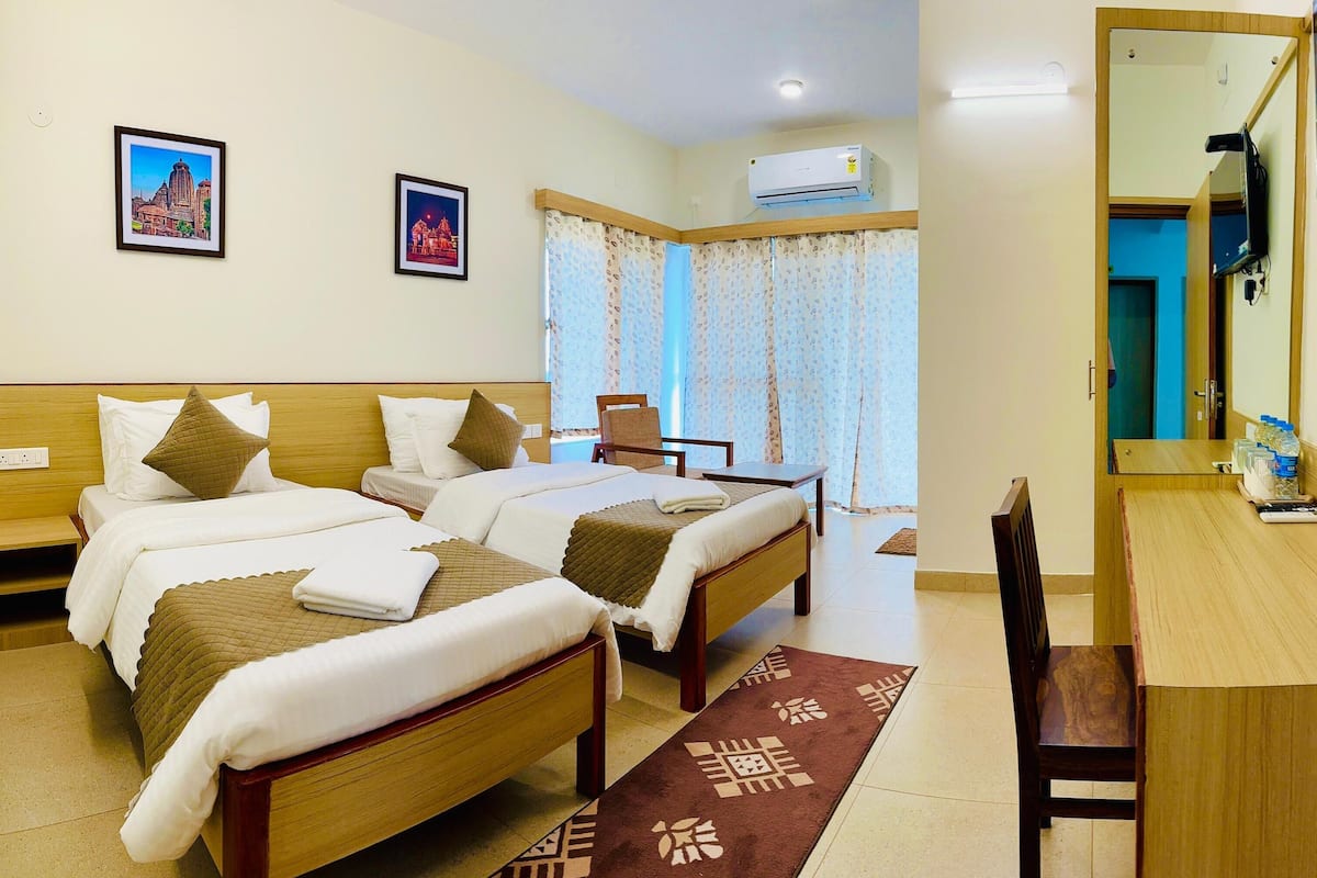 A hotel room with two beds, a desk, a chair, a mirror, and two framed pictures on the wall.