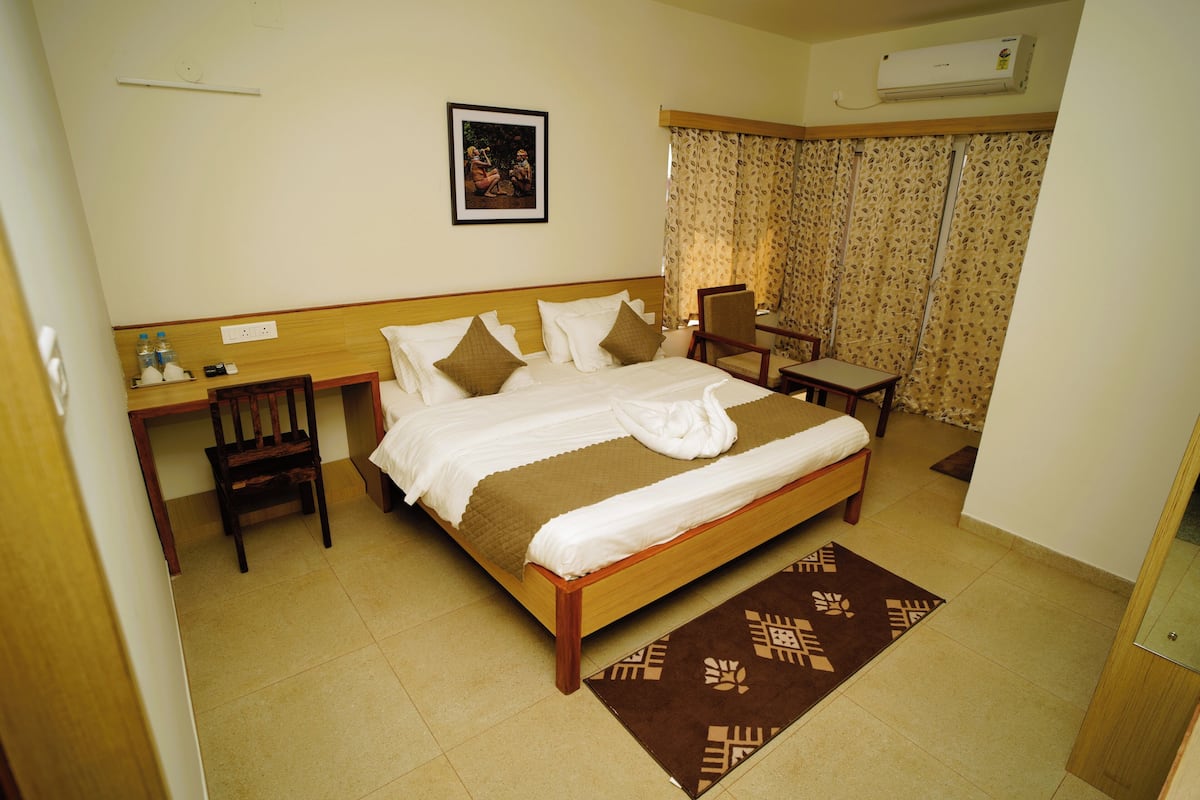 A hotel room with a bed, a desk, a chair, a small table, and a window with curtains.