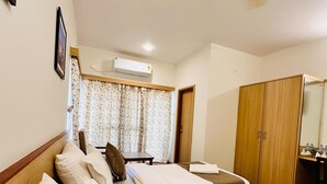 Ein Hotelzimmer mit zwei Einzelbetten, einem Holzschrank, einem Deckenventilator und einer Klimaanlage.