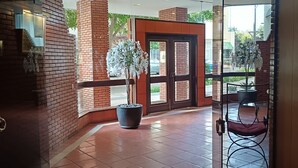 L'ingresso di un hotel con pavimento piastrellato, una porta in vetro, una pianta in vaso e una sedia a dondolo in metallo.