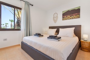 A bedroom with a bed, a window with curtains, a wall-mounted artwork, and a bedside lamp.