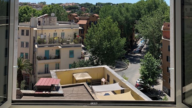 A view from a window of a building with multiple floors, balconies, and a street with parked cars and trees. - Iberia 80 (Roma)