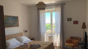 A bedroom with a bed, a chair, a desk, a lamp, and a window with curtains. - Iberia 80 (Roma)