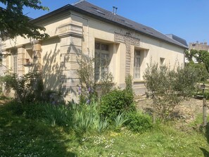 A building with a stone facade, a balcony with a lattice, and a garden with various plants and flowers. - Tiers lieu de l'Ermitage, Room 1 (Versailles)
