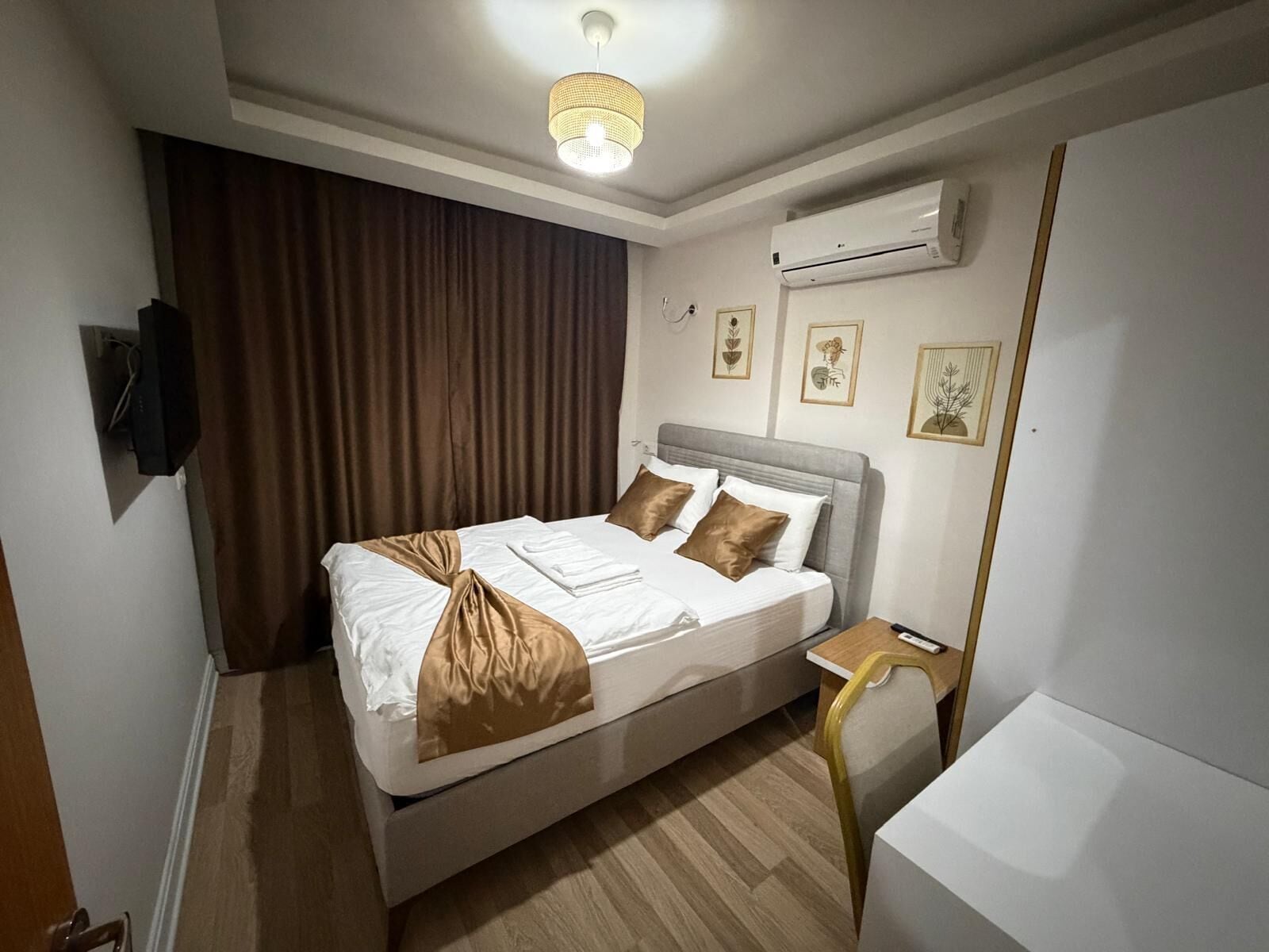 A neatly arranged hotel room with a bed, a bedside table, an air conditioning unit, and a ceiling light fixture.
