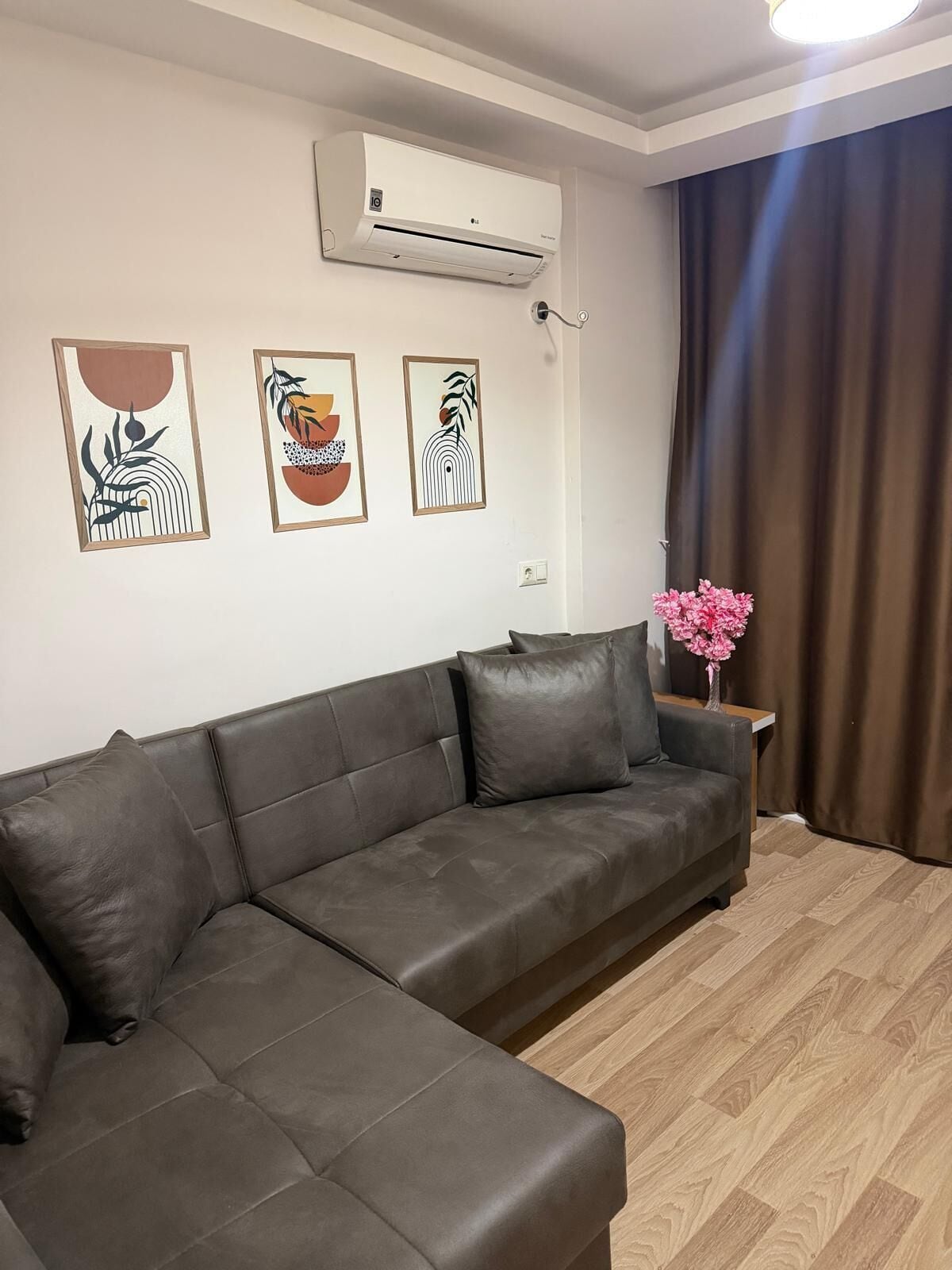 Un salon avec un canapé en cuir marron, un appareil de climatisation et trois œuvres d’art encadrées accrochées au mur.