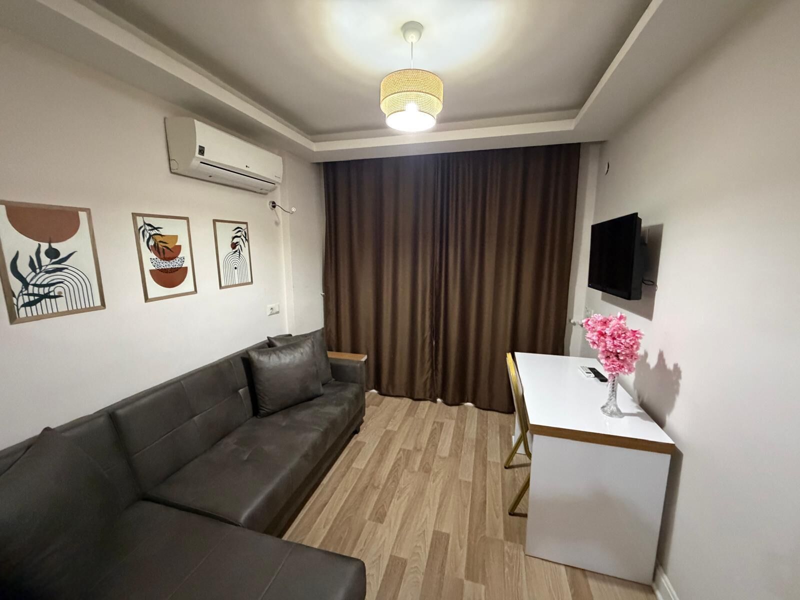 Ein modernes Wohnzimmer mit einer Ledersofa, einem kleinen Tisch mit einer Vase, einem Wand-Fernseher und Kunstwerken an der Wand.