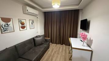 Ein modernes Wohnzimmer mit einer Ledersofa, einem kleinen Tisch mit einer Vase, einem Wand-Fernseher und Kunstwerken an der Wand.