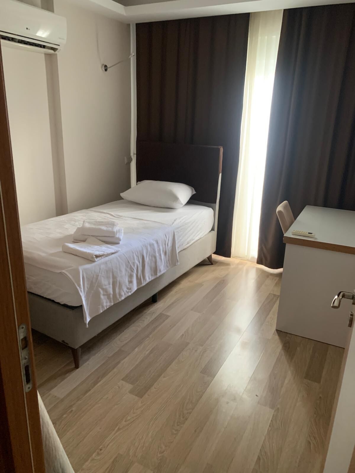 Um quarto pequeno e bem arrumado, com uma cama, mesa de cabeceira e guarda-roupa.