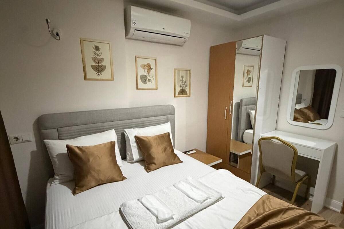 A hotel room with a bed, a desk, a chair, an air conditioner, and wall-mounted artwork.