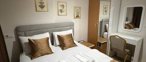 A hotel room with a bed, a desk, a chair, an air conditioner, and wall-mounted artwork.