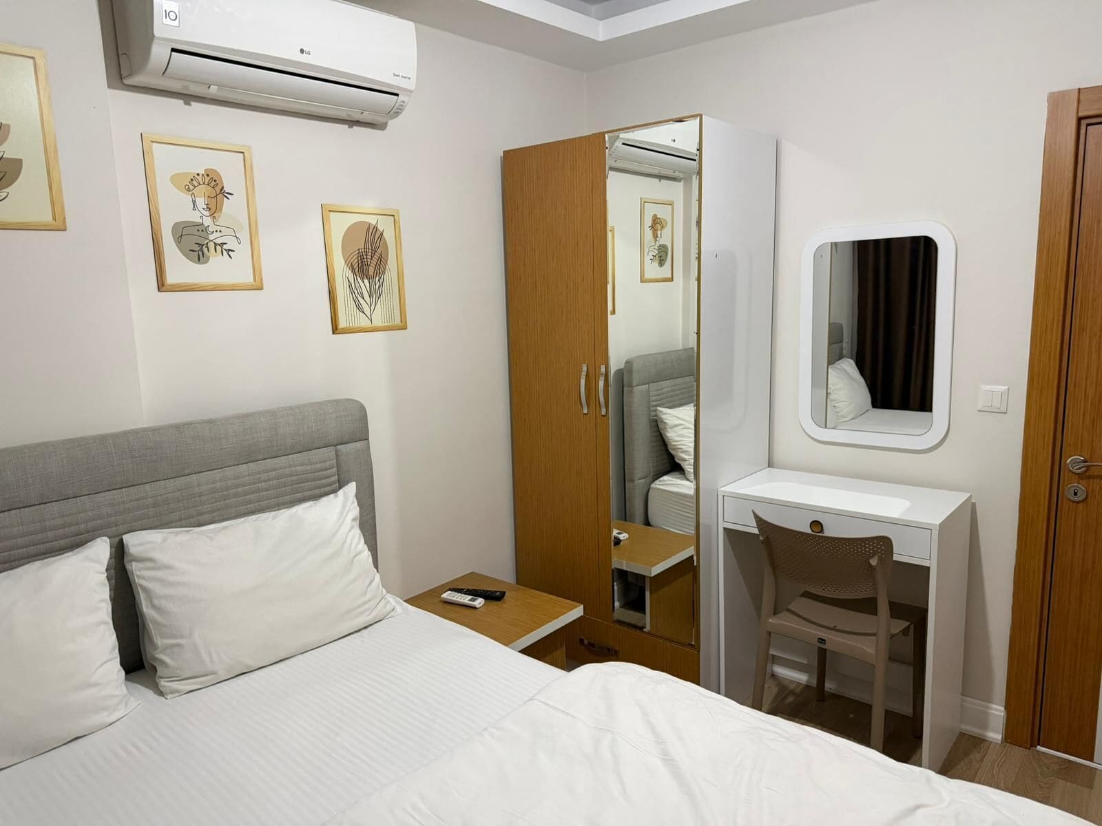 Quarto de hotel com cama, escrivaninha, cadeira, guarda-roupa, espelho e ar-condicionado.