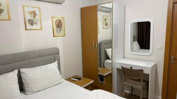 Quarto de hotel com cama, escrivaninha, cadeira, guarda-roupa, espelho e ar-condicionado.