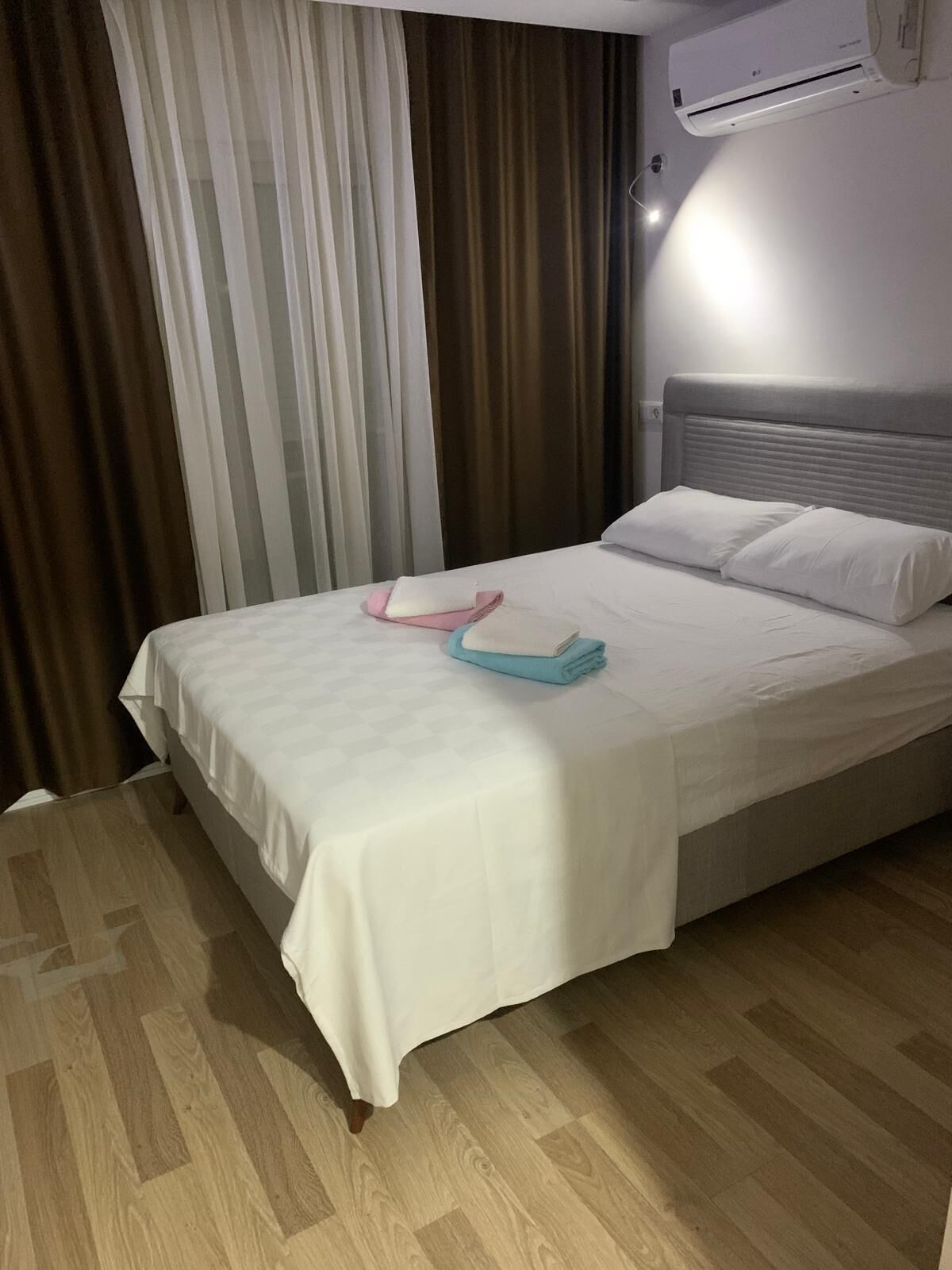 Ein Hotelzimmer mit Bett, weißer Bettwäsche, einem gefalteten Handtuch und einer Klimaanlage an der Wand.