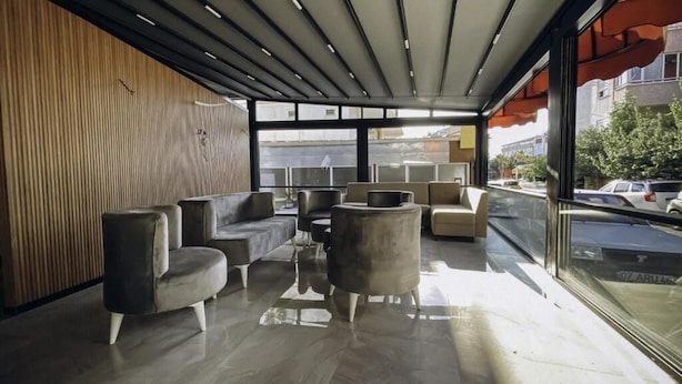 A modern interior with a seating area featuring sofas and a round table, large windows offering a view of the street, and a wooden wall. - Nativo Hotel (Antalya)