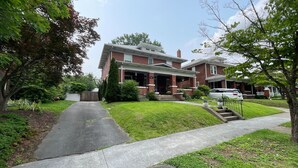 A two-story brick house with a front porch, a visible garage, and a well-maintained lawn. - City Vibes + Nature Trails! Relax in our comfy 2BR—perfect base for exploring Johnson City & beyond. (Johnson)