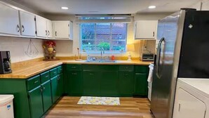 A kitchen with green cabinets, a wooden countertop, a stainless steel refrigerator, and a window with a view of greenery. - City Vibes + Nature Trails! Relax in our comfy 2BR—perfect base for exploring Johnson City & beyond. (Johnson)